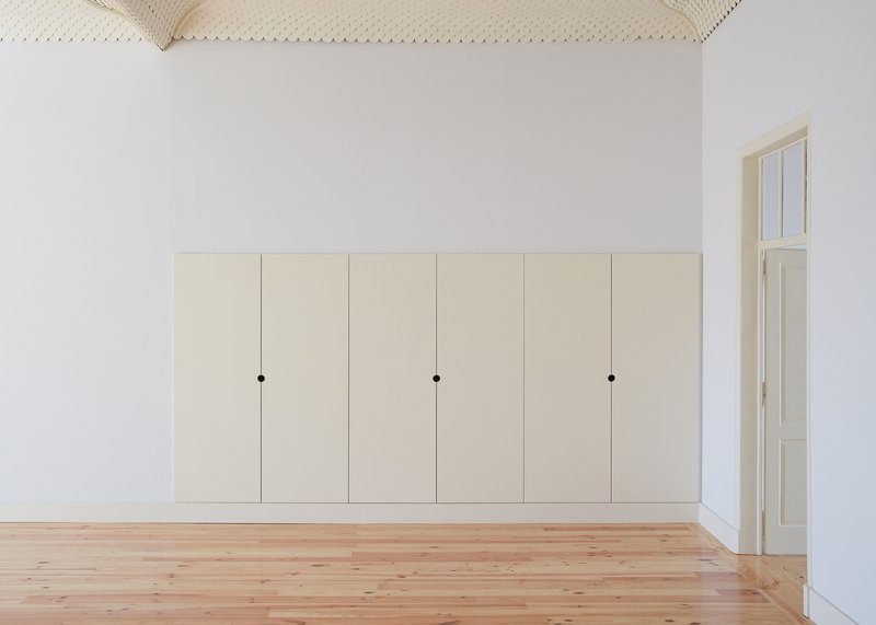 Built-in cream wardrobe with six panel doors against white walls and vaulted woven reed ceiling