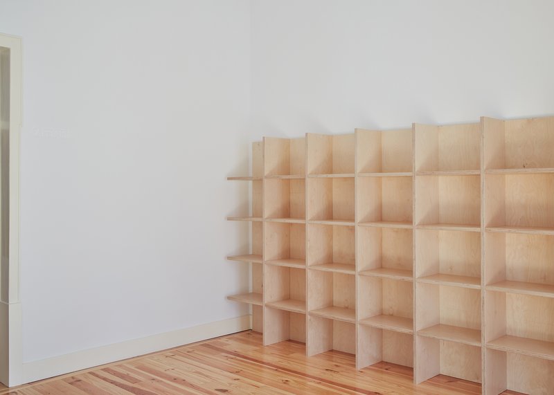Built-in plywood shelving grid along a white wall with natural wood flooring