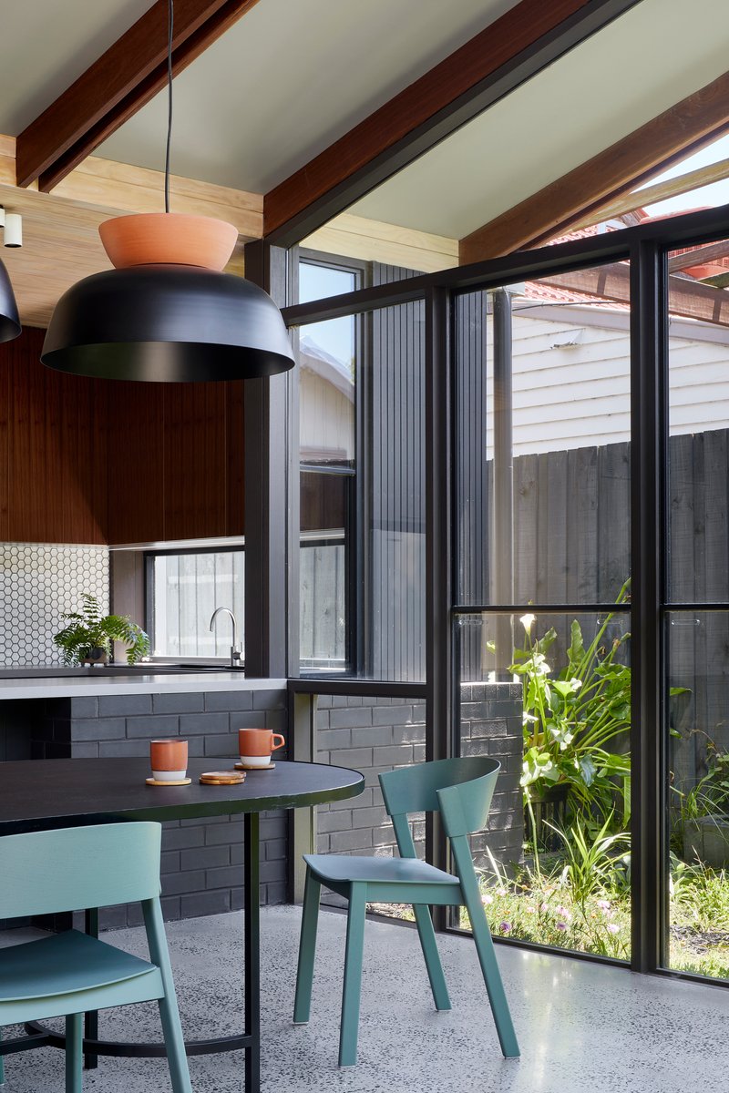 Dining area with exposed timber beams and floor-to-ceiling glazing overlooking planted courtyard in daylight