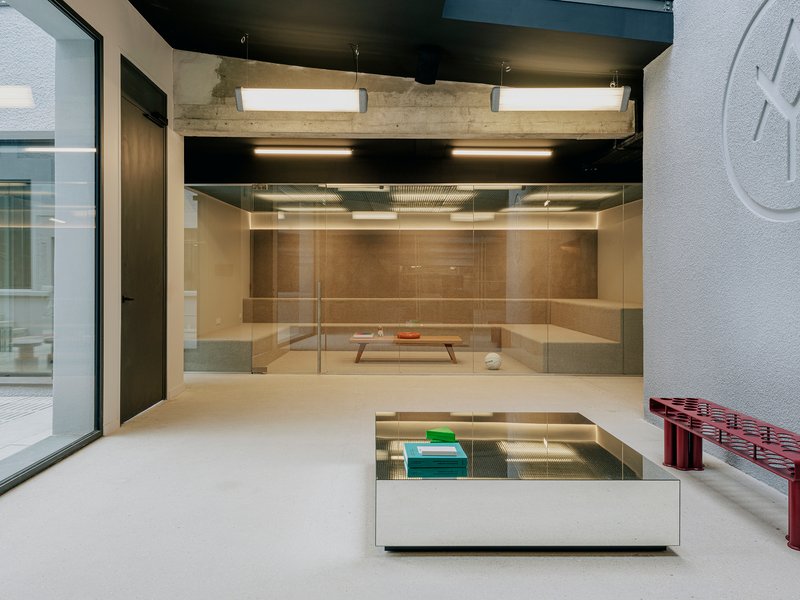 Interior gallery space with exposed concrete beams, black ceiling, glass vitrine, and views to courtyard beyond