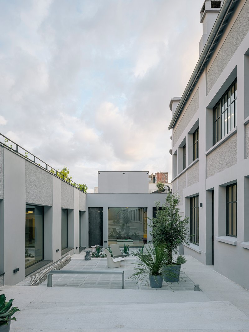 Courtyard with light grey pavers and planted beds between white rendered walls under cloudy dusk sky