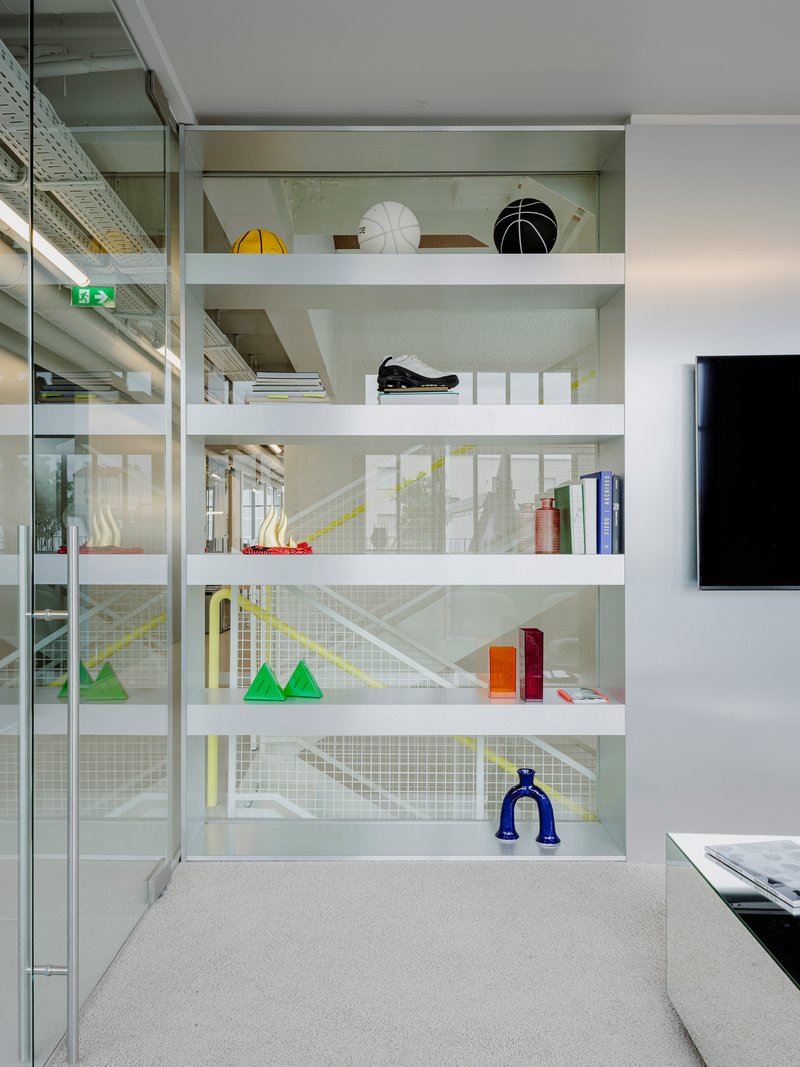 White shelving unit displaying colorful objects behind wire mesh panels with glass partitions beyond