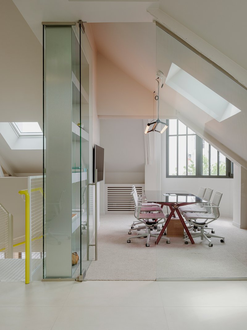 Attic meeting room with sloped ceilings, skylights, and glass partition separating workspace below