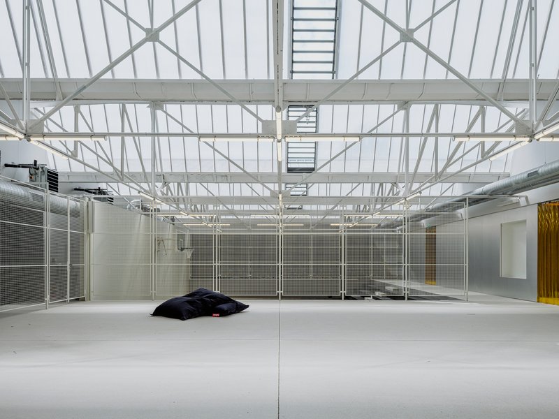 Large hall with white painted steel roof trusses, skylights, mesh partitions, and polished resin floor