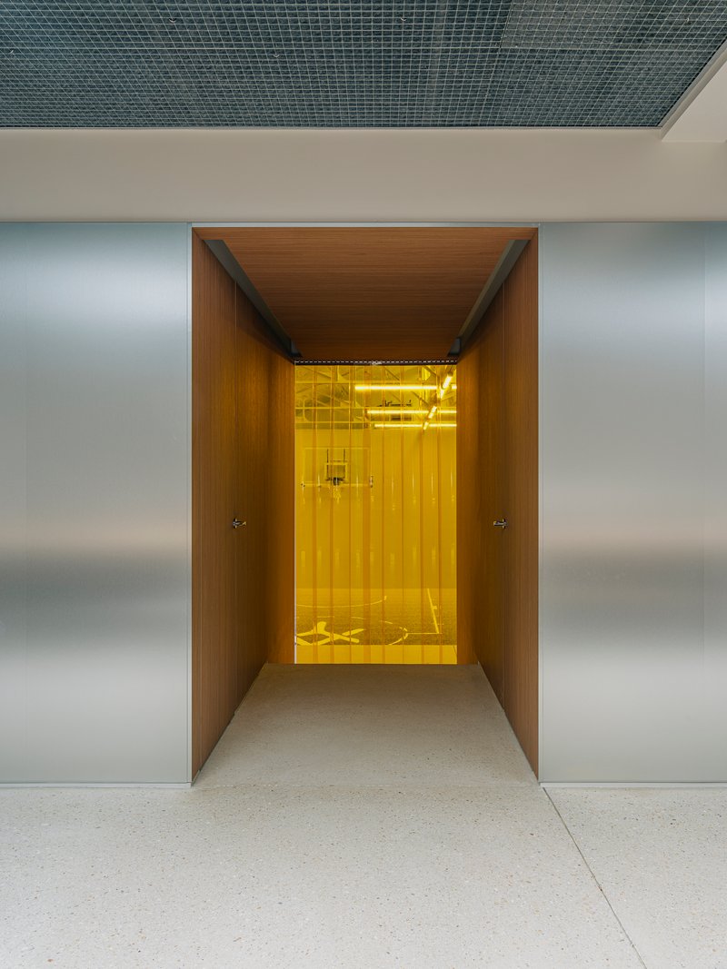 Wood-lined corridor leading to a yellow-lit elevator vestibule framed by brushed metal walls