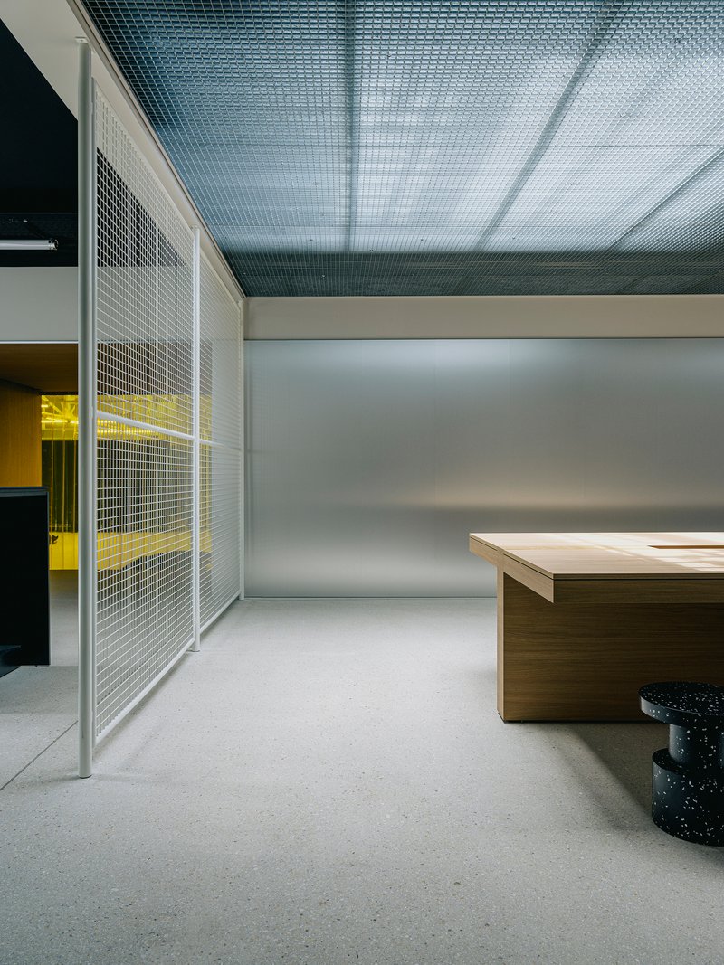 Interior space with metal mesh partition panels and yellow-lit room visible beyond timber desk