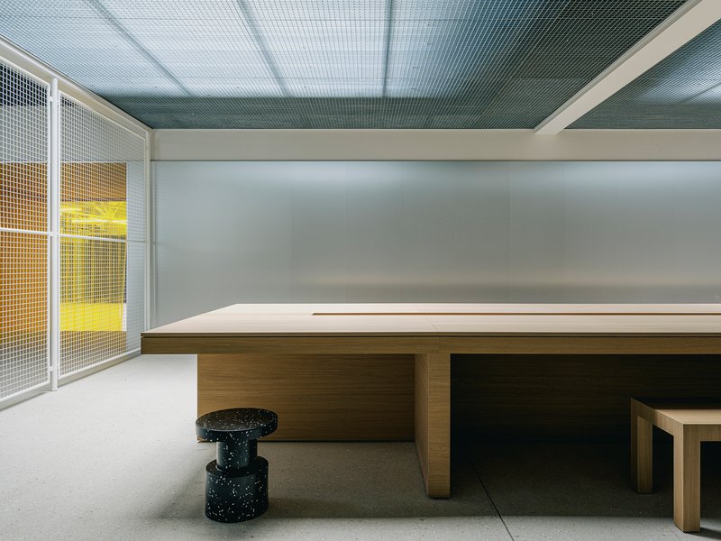 Timber conference table with terrazzo cylinder stools beneath a translucent gridded ceiling