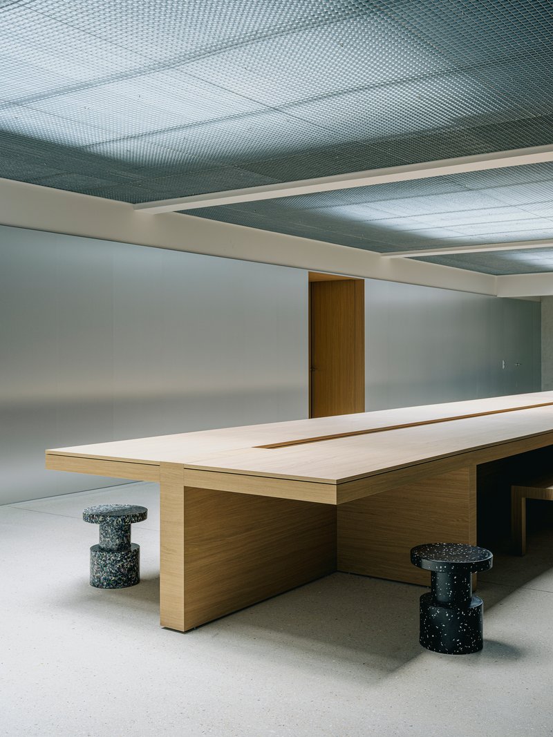 Close-up of the timber table edge with speckled terrazzo stools under recessed ceiling panels