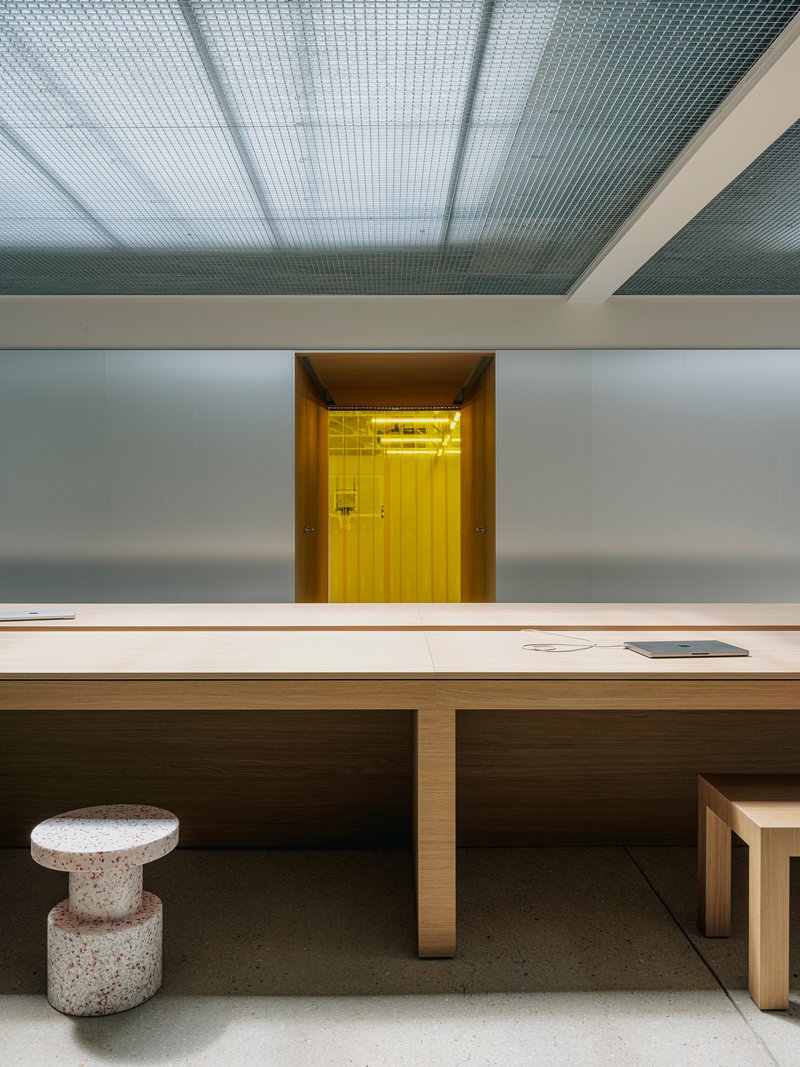 View across the table surface toward yellow-lit doorway with terrazzo stool in foreground