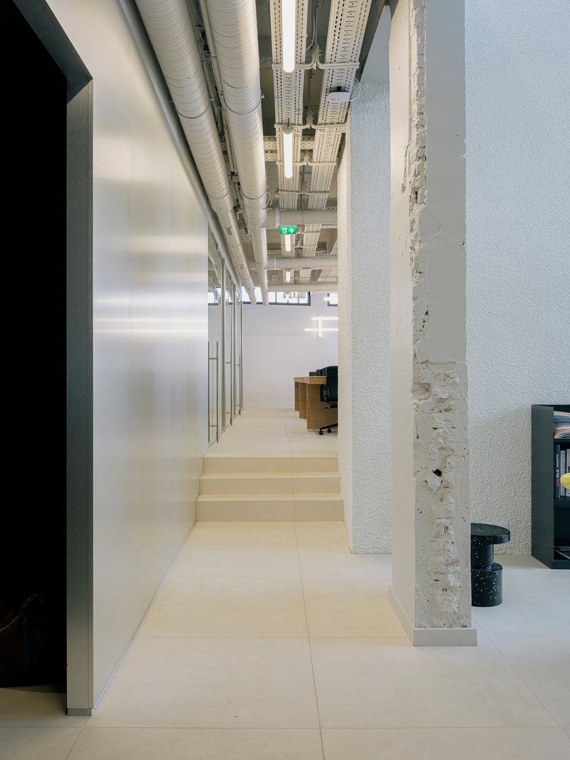 Wide interior steps rising between white concrete column and glazed partition with exposed ductwork above