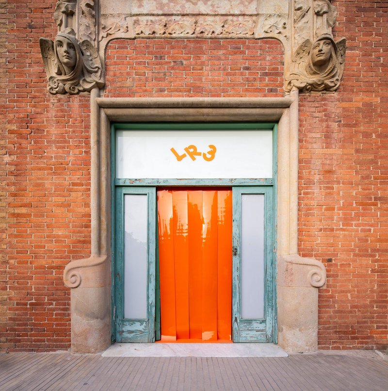 Ornate brick facade entrance with carved stone surround and orange vertical slats behind glass doors
