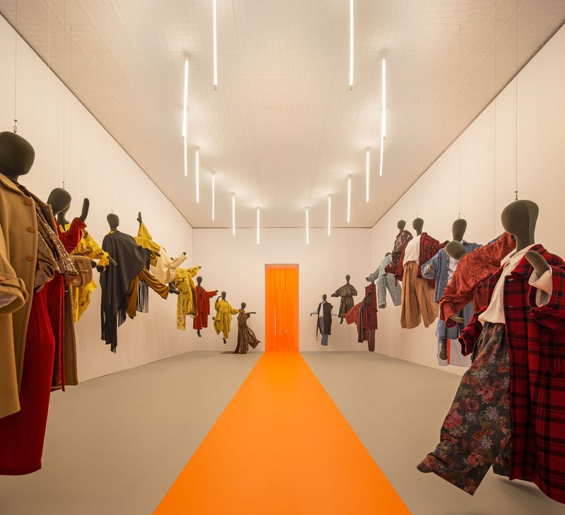 Long view of the exhibition hall with wall-mounted textile displays and vertical tube lighting in the ceiling