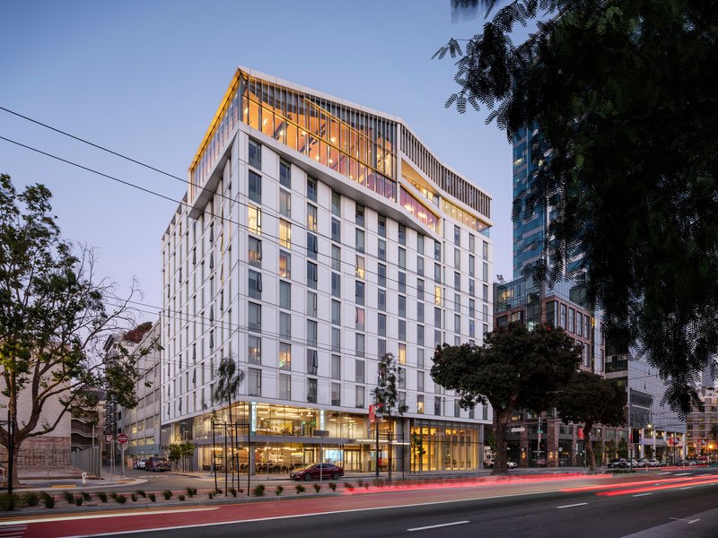 Street view of the white paneled facade with vertical fins screening the illuminated upper level at dusk