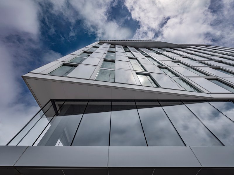 Upward view of a cantilevered facade with white and glass panels against cloudy sky
