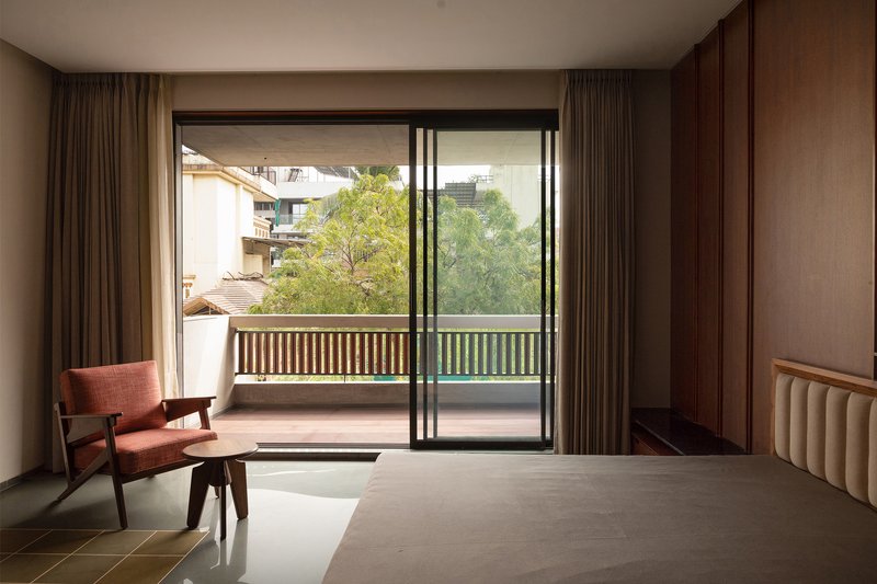 Bedroom opening to a balcony with slatted railing and treetops beyond the sliding glass doors