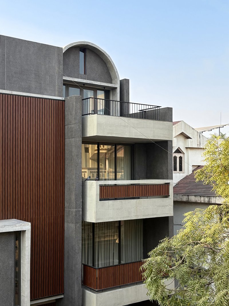 Street view of the layered concrete and timber-slatted facade with arched vault and cantilevered balconies