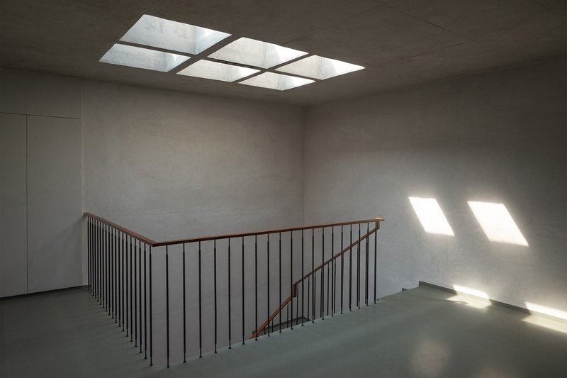 Stairwell landing with grid skylight washing concrete walls and floor with natural light