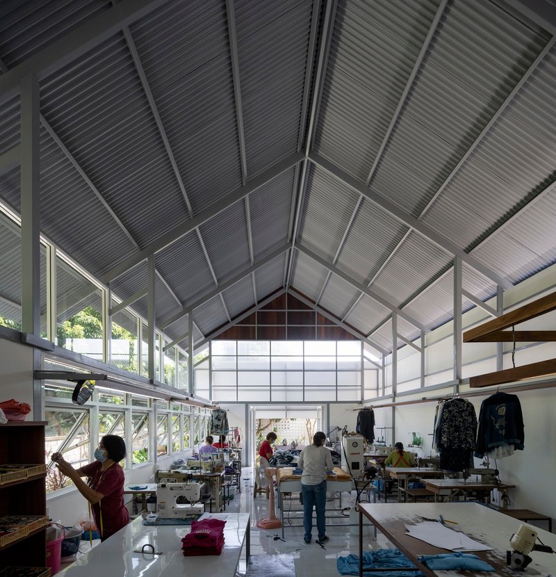 Workshop floor with sewing stations and workers under the steel-framed gabled ceiling with corrugated cladding