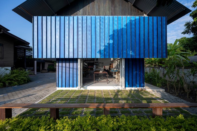 Blue corrugated metal volume with folding glass doors opening onto a gridded paver and grass courtyard
