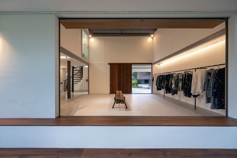 View through wide timber-framed opening showing the studio interior with clothing racks and spiral stair