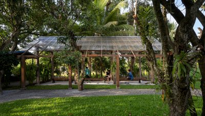 This architectural image showcases an open-air pavilion nestled within a lush, tropical landscape. T