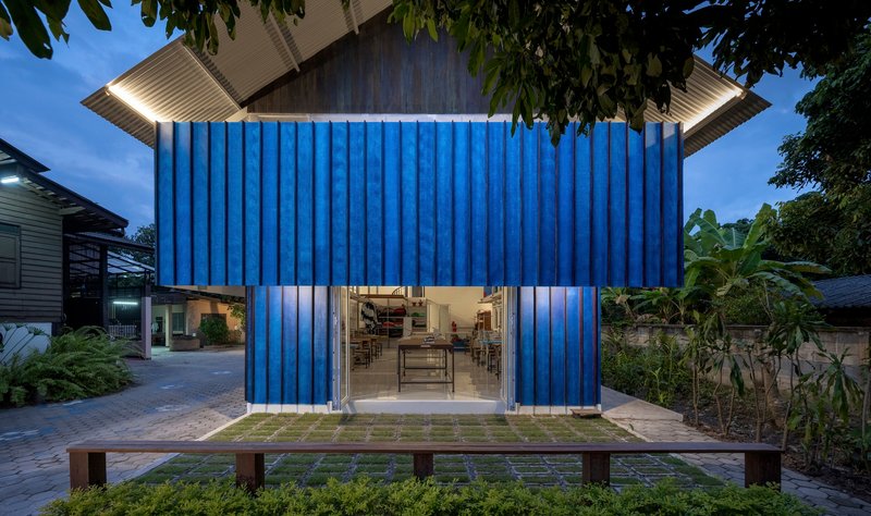 Blue corrugated facade with central glazed opening and timber bench at dusk