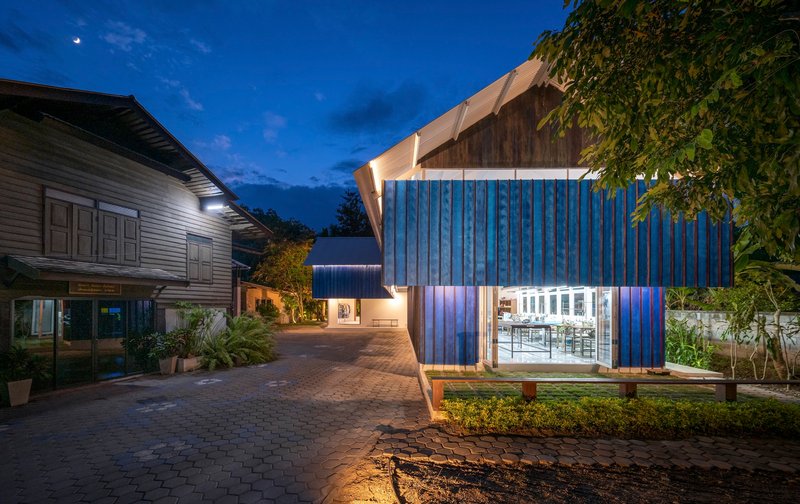 Illuminated pavilion with ribbed blue walls and upswept roof under evening sky
