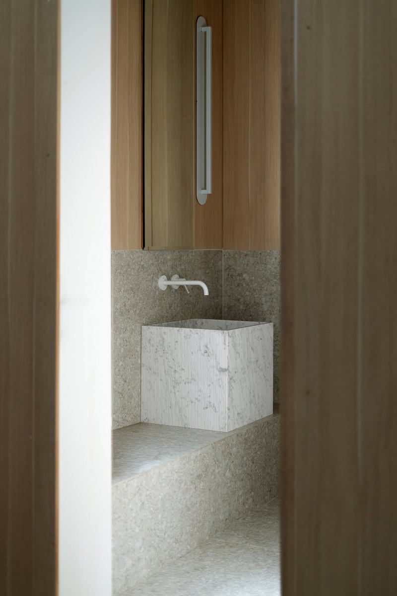 View through timber sliding door to a textured stone bathroom with floating white mosaic basin