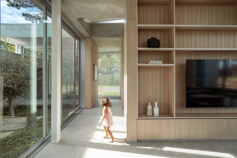 Interior corridor with timber shelving and a child walking toward glazed courtyard opening