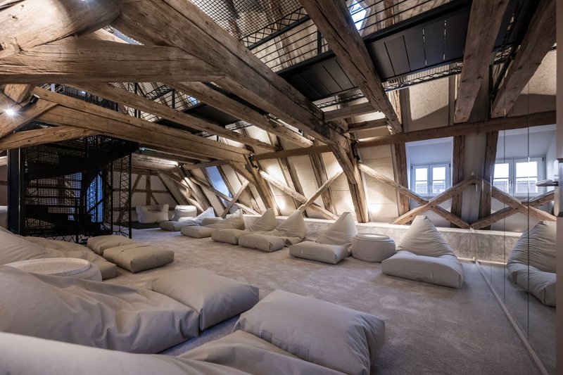 Attic relaxation room with exposed diagonal timber beams and floor cushions scattered on polished concrete