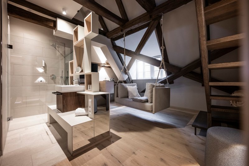 Open bathroom with glass shower enclosure and exposed timber trusses cutting diagonally through the volume