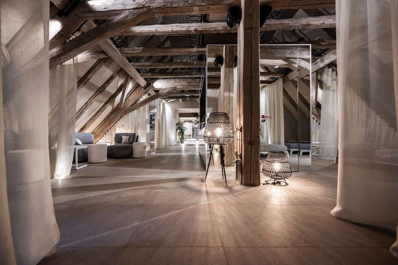 Attic interior with exposed timber trusses, concrete columns, and wicker pendant lights along a polished floor