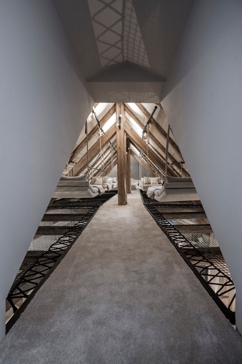 Central concrete walkway flanked by metal mesh decking under symmetrical timber roof trusses