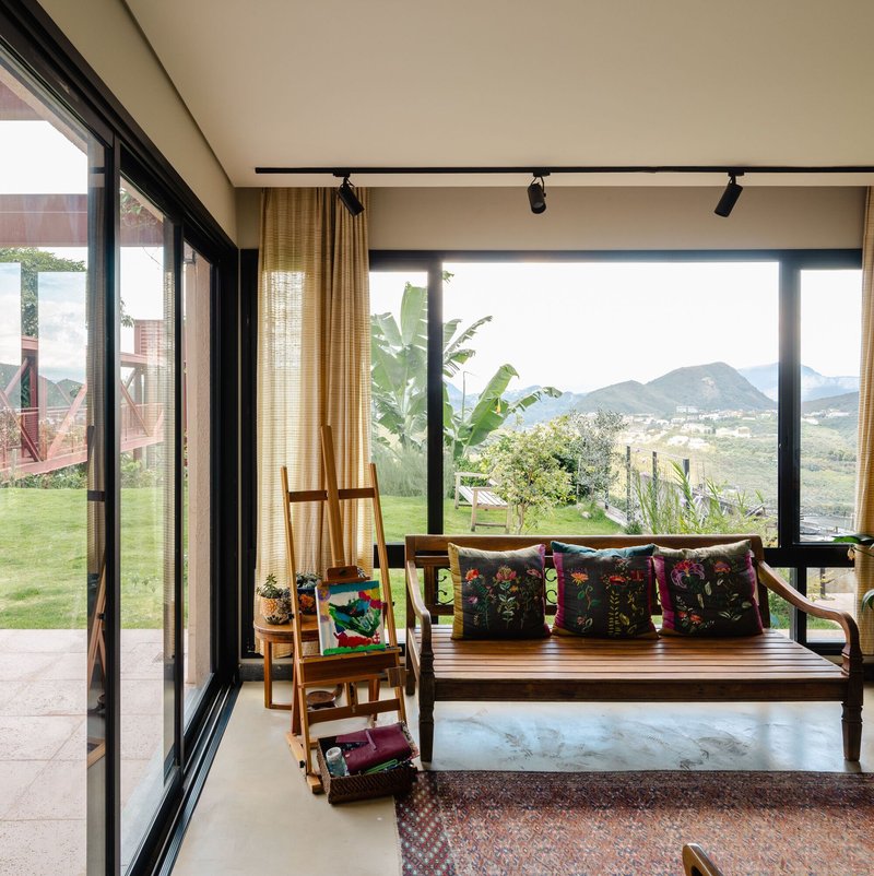Floor-to-ceiling windows framing a hillside view with banana plants and mountains in the distance