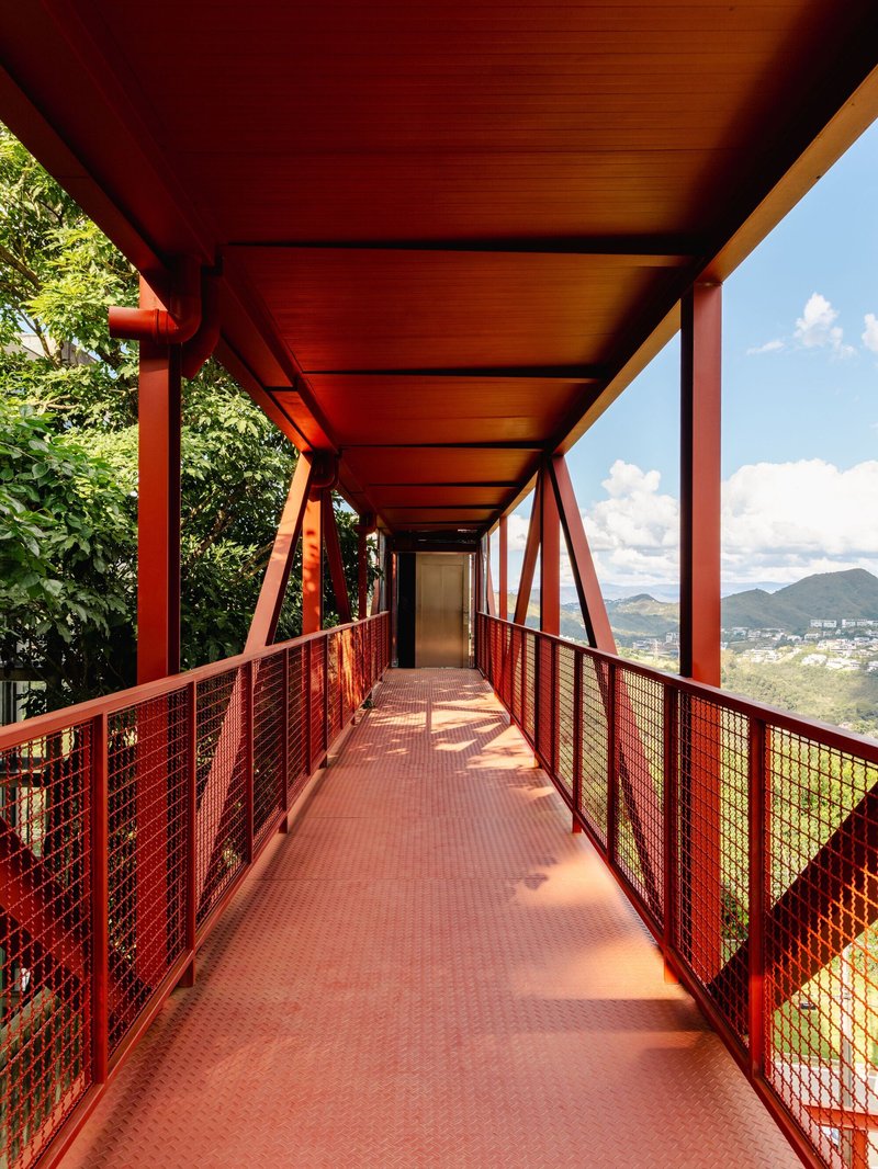 Covered bridge corridor with red steel mesh railings and perforated metal flooring casting shadows below