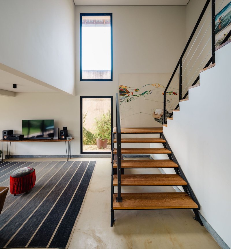 Double-height living room with open-tread timber staircase and tall vertical windows framing a planted courtyard