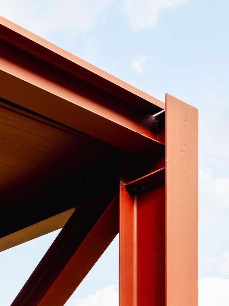 Close-up of painted steel beam joint and exposed timber roof structure against a clear sky