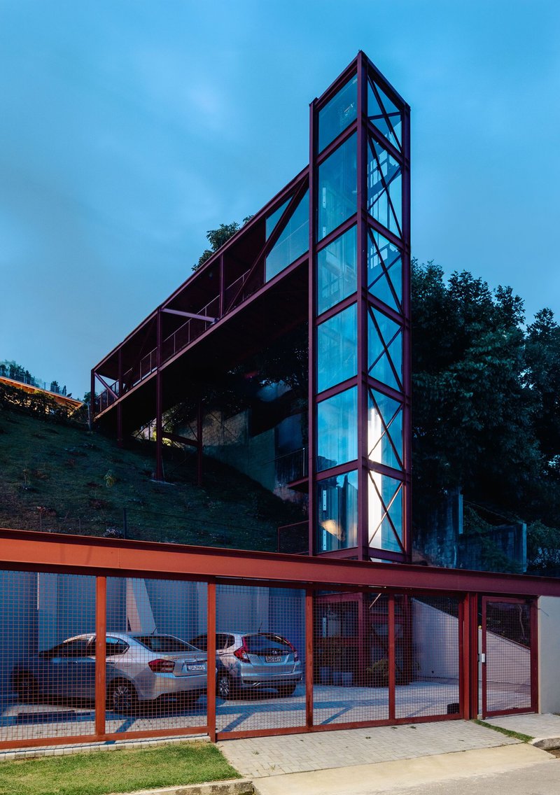 Street view of the red steel-framed tower rising above the mesh-fenced carport at dusk