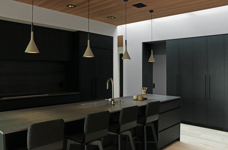 Kitchen island with black cabinetry and brass pendant lights beneath wood ceiling