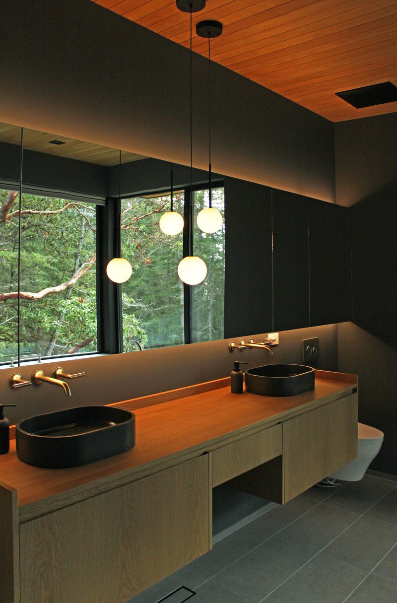 Bathroom vanity with timber counter and pendant globe lights facing forest through floor-to-ceiling glazing