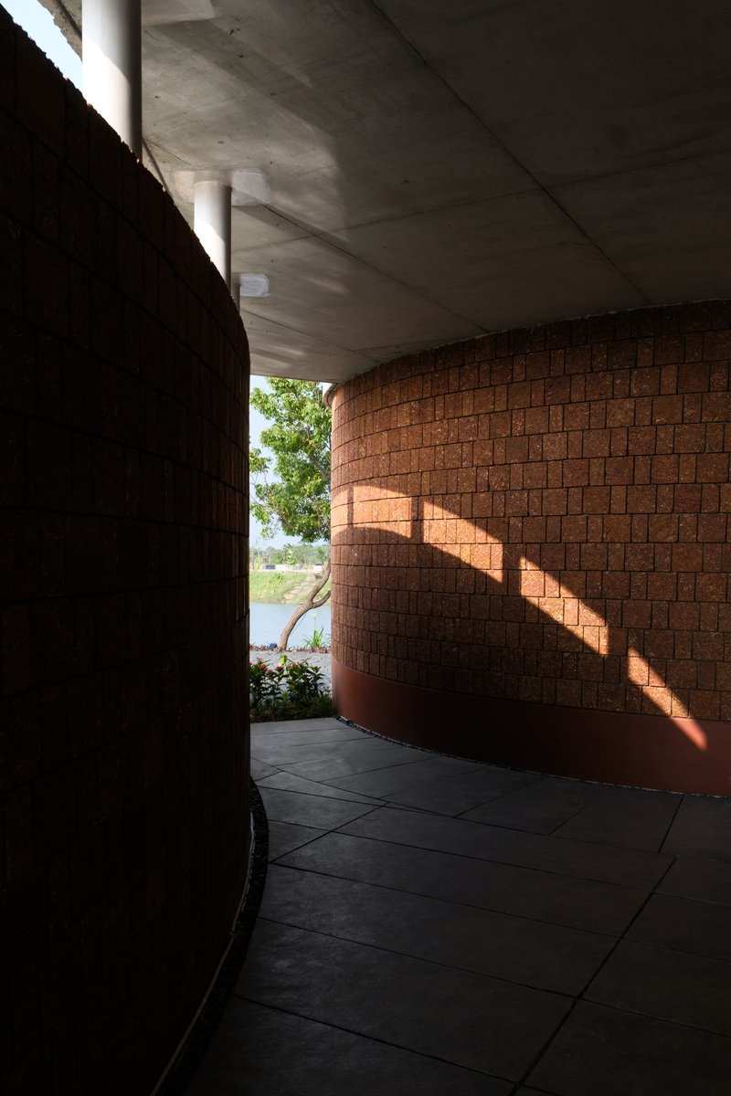 Curved interior corridor with laterite brick wall receiving striped sunlight through clerestory opening