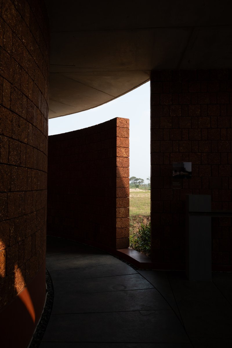 Interior corridor with curved concrete ceiling and compressed earth block walls framing a view to the landscape