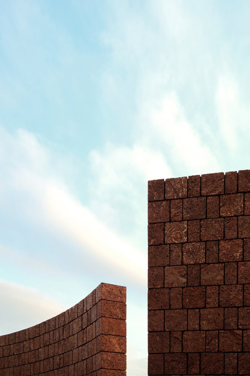 Upward view of curved compressed earth block walls meeting against a pale sky