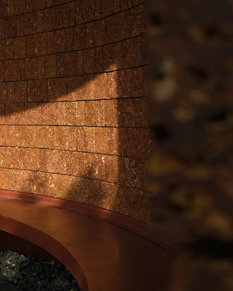 Detail of compressed earth block wall above a curved metal base in warm sunlight