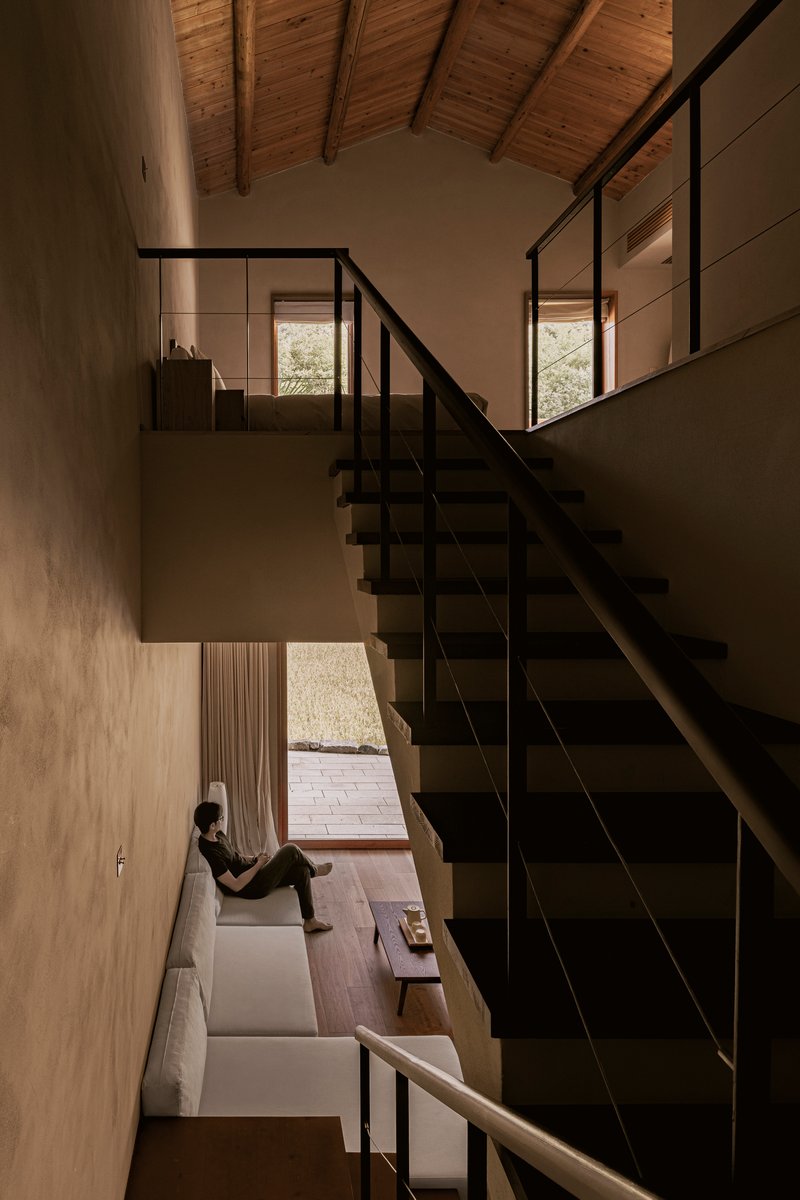 Double-height space with black steel stair and person seated by window below