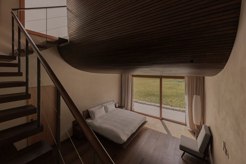 Bedroom with curved timber slat ceiling, steel staircase and glass door opening to a grassy courtyard