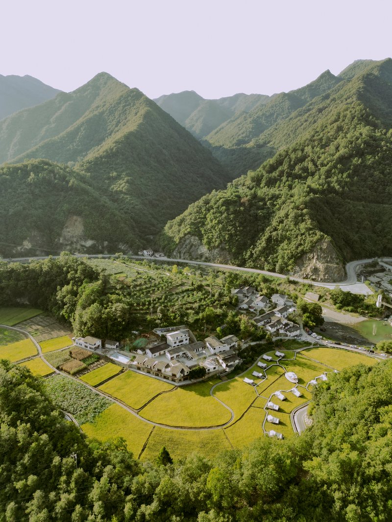 Aerial view of the compound nestled between terraced rice paddies and a winding mountain road