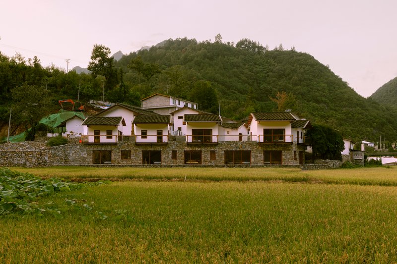 Front elevation showing repeated gable volumes above a continuous stone retaining wall at dusk