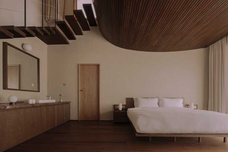 Bedroom interior with curved timber slat ceiling, cantilevered stair treads, and dark wood flooring