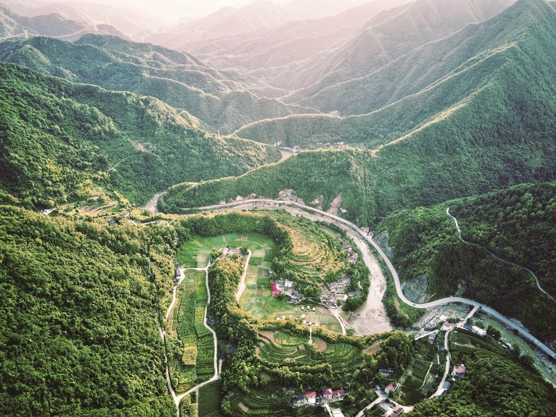 Aerial view of terraced buildings and winding roads set within a forested mountain valley at dusk